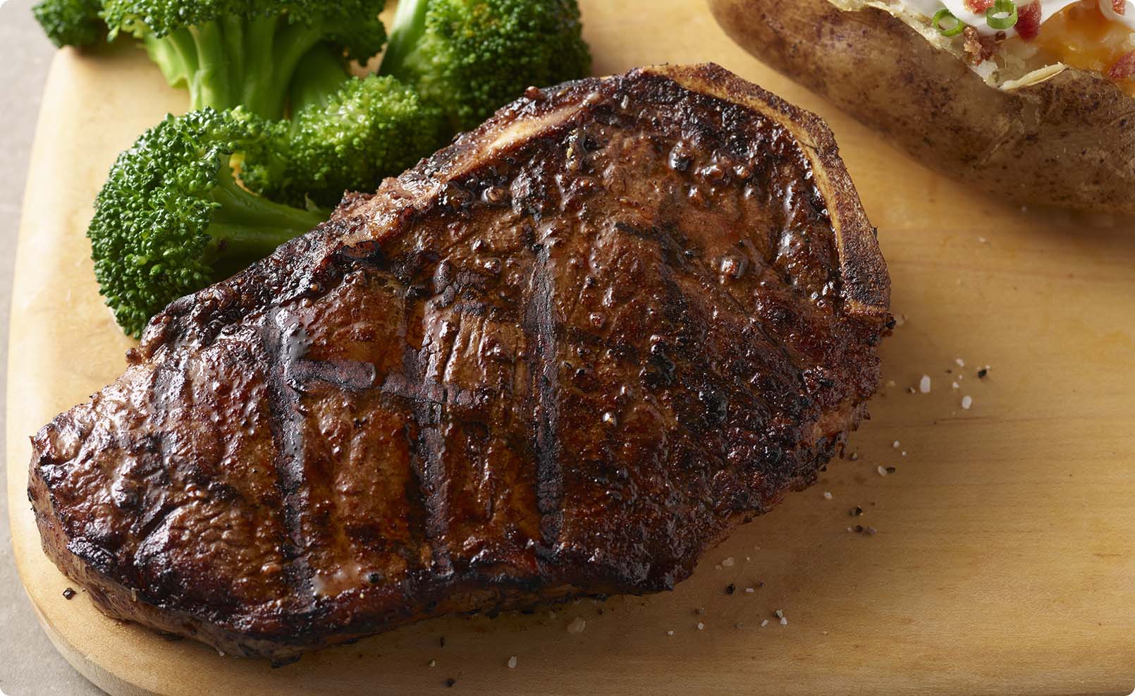 A hand-cut Prime bone-in NY strip steak, with crisp, charred edges. Flakes of salt sprinkled atop the dark brown cut.