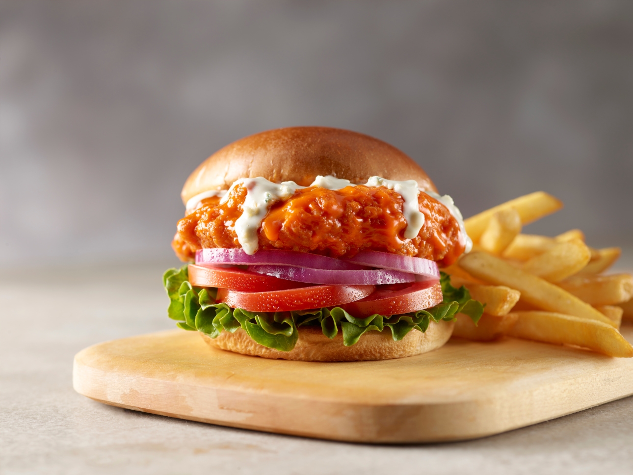 A toasted bun with breaded chicken tossed in buffalo sauce, paired with blue cheese dressing, lettuce, tomato, and onion.
