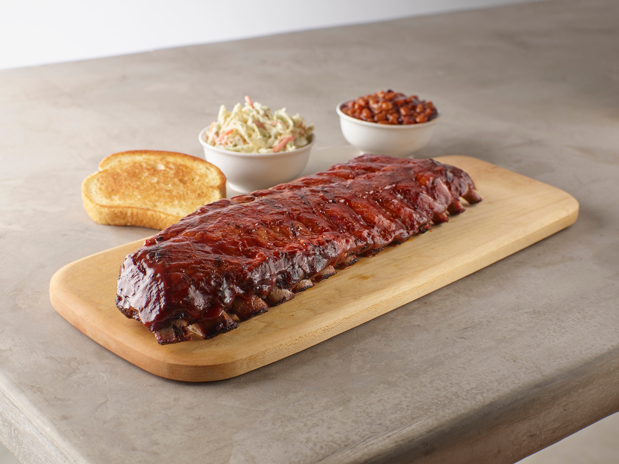 A larger-than-life rack of juicy ribs, served with garlic bread, coleslaw, and BBQ baked beans.