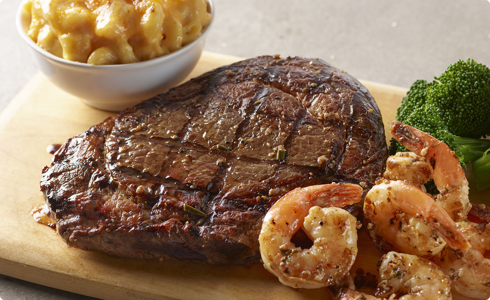 A 14oz. fire-grilled, juicy ribeye with a crispy, dark crust on the edges. Sides of shrimp, broccoli, and mac and cheese.